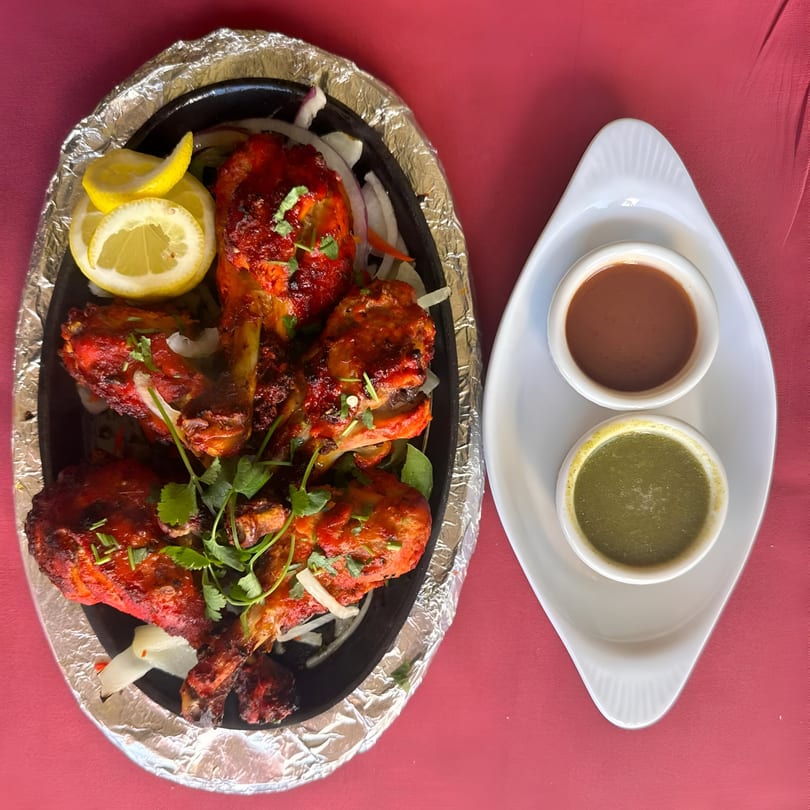Indian Spice Bistro's Tandoori Chicken with lemon slices, onions, and two dipping sauces on a red tablecloth.