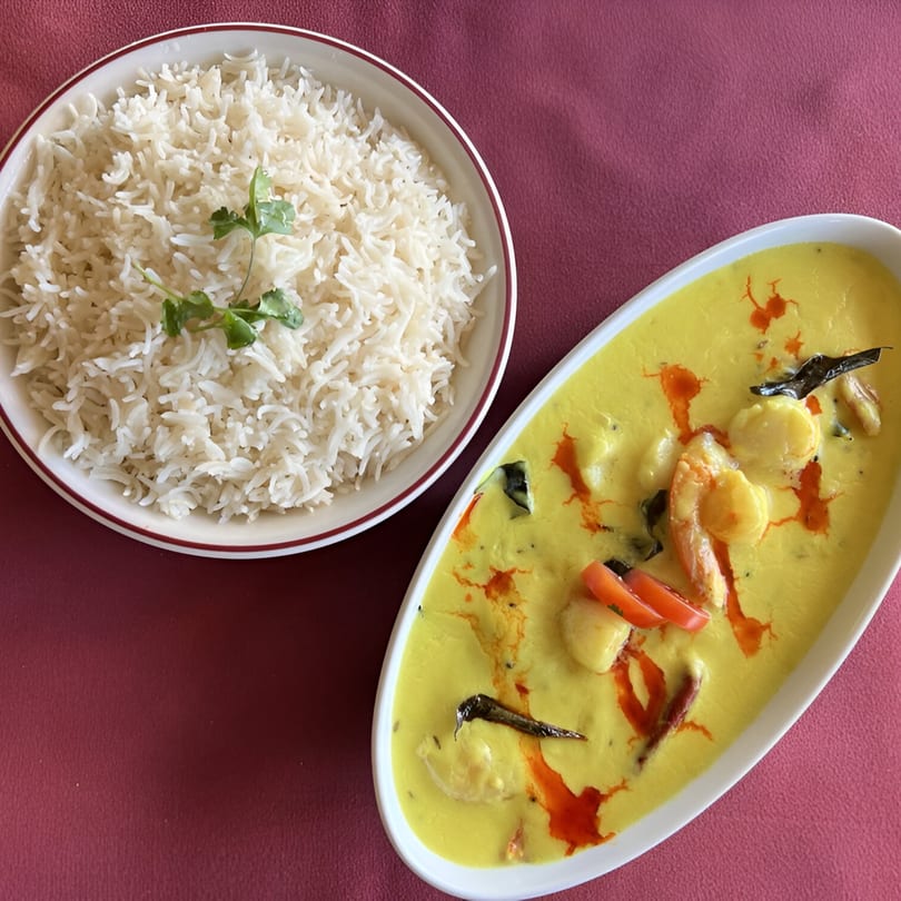 Indian Spice Bistro's shrimp curry with rice, garnished with cilantro, on a red tablecloth.