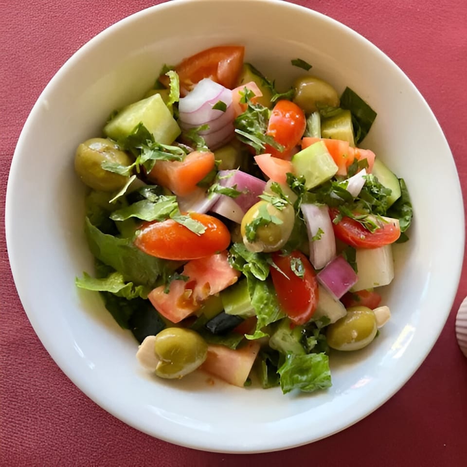 A fresh Indian salad with lettuce, tomatoes, cucumbers, red onions, and green olives.