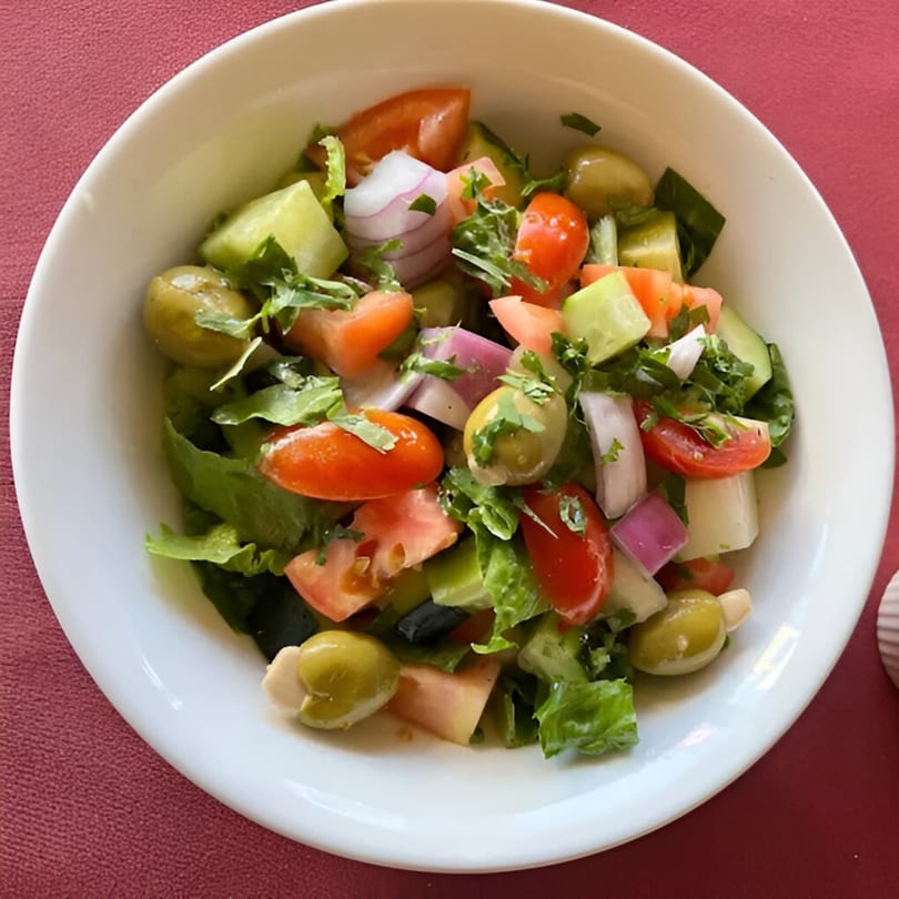 A fresh Indian salad with lettuce, tomatoes, cucumbers, red onions, and green olives.