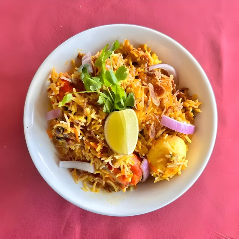 Indian Spice Bistro's chicken biryani with rice, onions, cilantro, and a lime wedge.