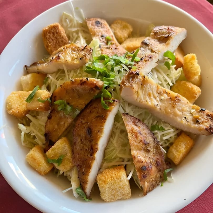 Grilled chicken pieces and croutons on a bed of shredded lettuce, garnished with fresh herbs.