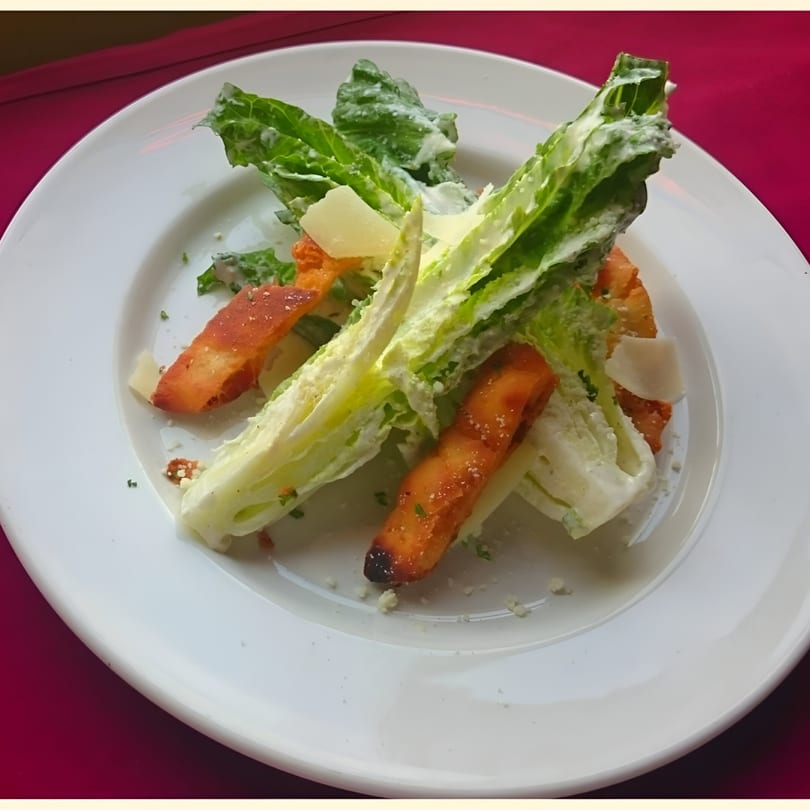 Caesar salad with romaine lettuce, croutons, and parmesan cheese on a white plate.