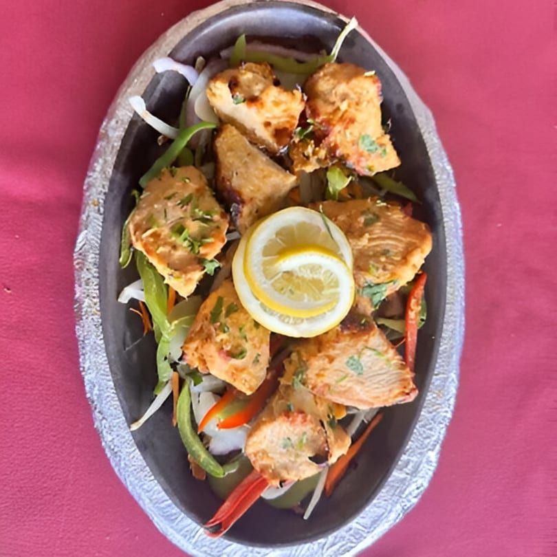 Indian Spice Bistro's chicken tikka, garnished with lemon slices and fresh vegetables, served in a black dish.